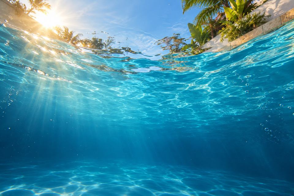 Vista de dentro da água de uma piscina, com a luz do sol entrando pela superfície.
